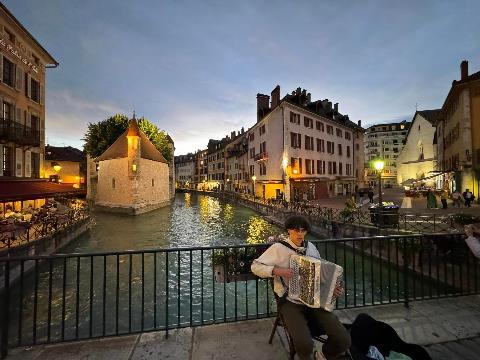 A person playing an instrument on a bridge over a canal Description automatically generated